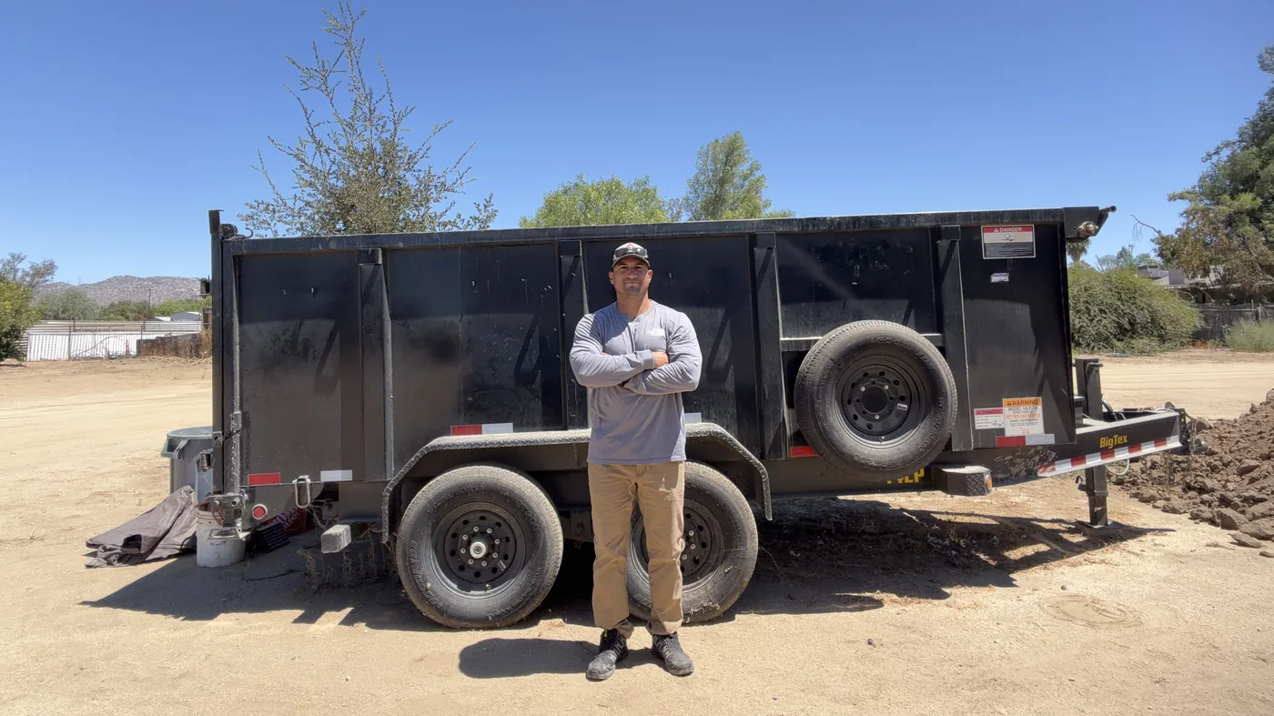 Owner of 1775 Junk Hauling standing beside the dump trailer on a job in Lake Elsinore