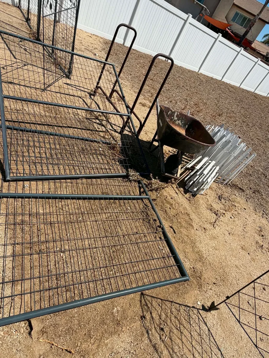 Wire fence panels, a rusted wheelbarrow, and stacked vinyl fencing loaded out on a Riverside County haul
