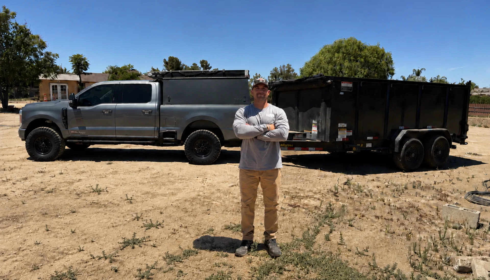 Owner of 1775 Junk Hauling standing between his truck and loaded dump trailer in Riverside County